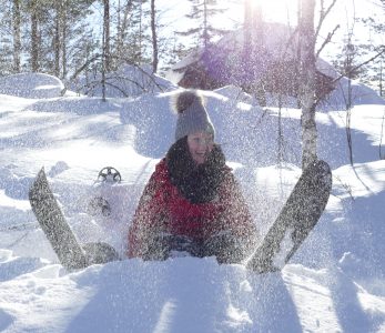 Tyttö istuu paksussa lumikinoksessa iloisena lumisukset jalassaan.