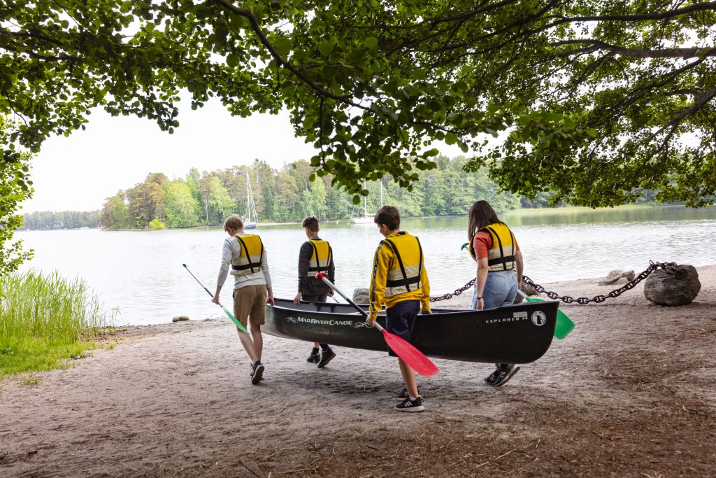 Neljä nuorta kantaa kanoottia rantaan.