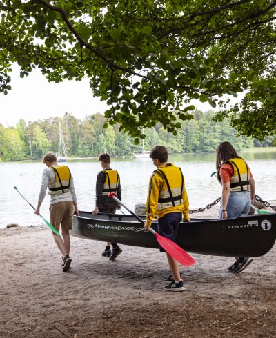 Neljä nuorta kantaa kanoottia rantaan.