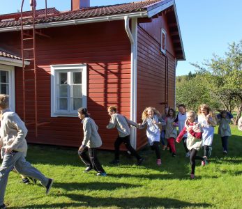 Lapsia juoksemassa vanhan ajan koulupuvuissa.