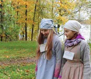 Kaksi tyttöä, joilla päällään vanhanajan koulupuvut.