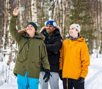 Kolme nuorta ottamassa selfietä lumisessa metsässä.