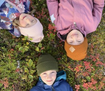 Kolme lasta makaa maassa ruskan seassa.