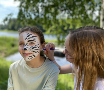 Kaksi nuorta tekee kasvomaalauksia toisilleen kesäleirillä.