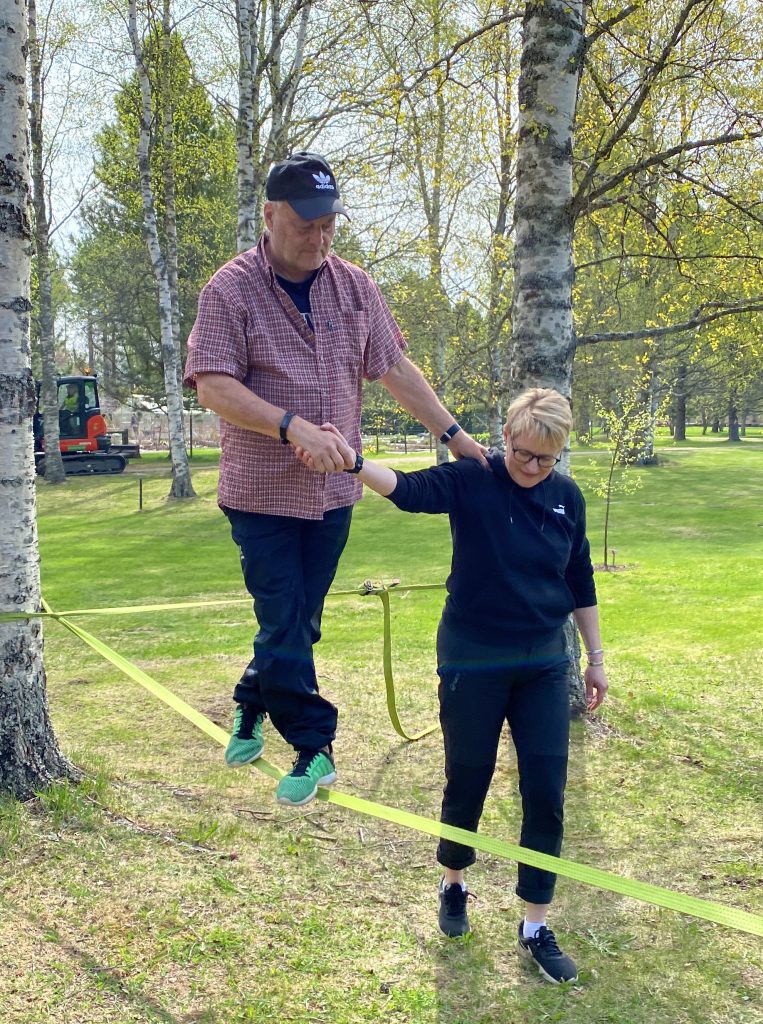 Mies kävelee alaköysiradalla ja ottaa tukea kaverista.