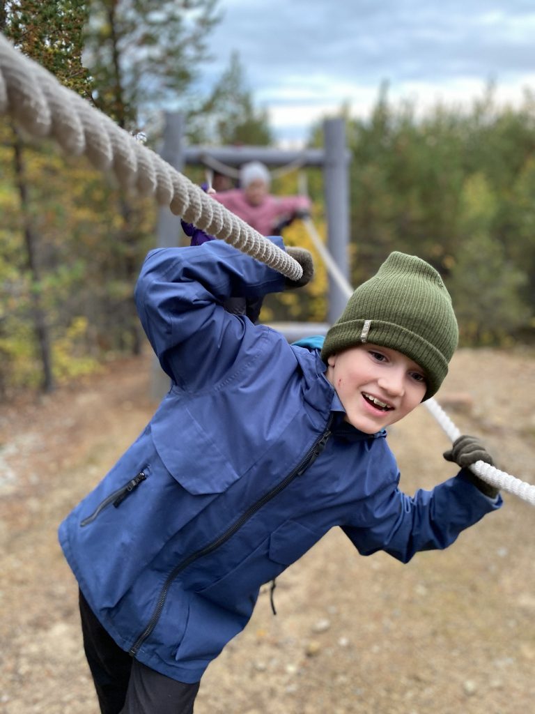 Poika kiipeilee alaköysiradalla jännittyneenä, mutta iloisena.